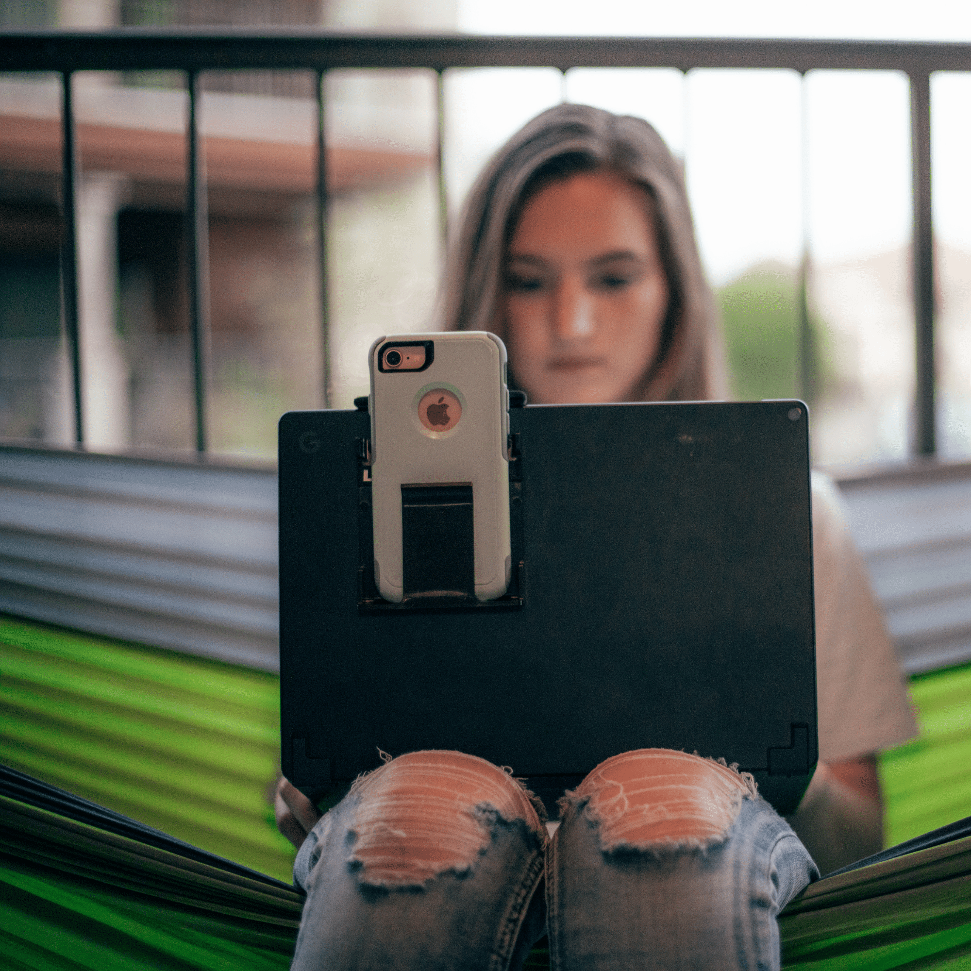 Image of woman using the Device Cady to hold her phone while she works on her laptop in a hammock.